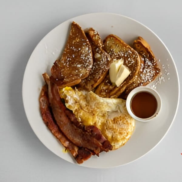 A breakfast plate with French toast, bacon, fried eggs, butter, and a side of syrup.