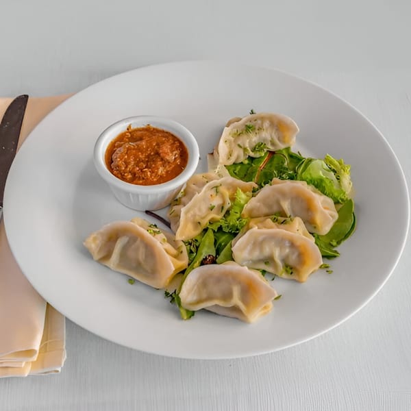 A plate of Lighthouse Bistro dumplings with a side of red dipping sauce and green salad.