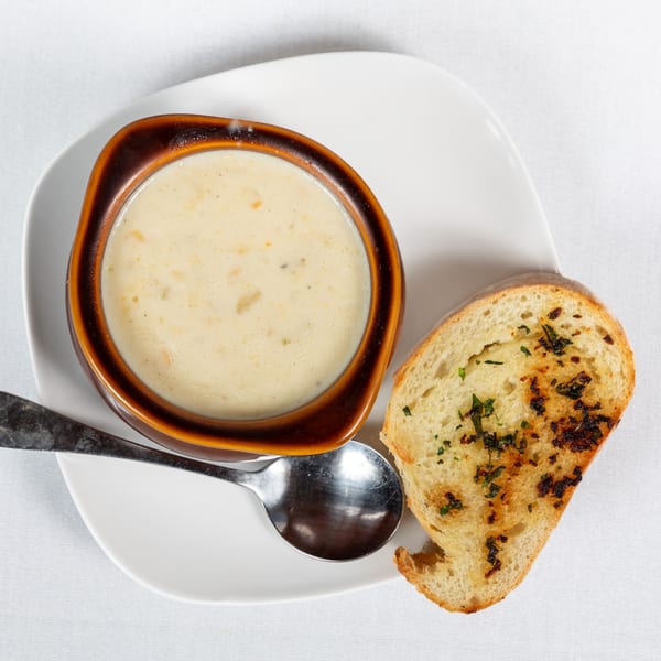 Creamy soup in a brown bowl with a spoon and a slice of toasted garlic bread on a white plate.