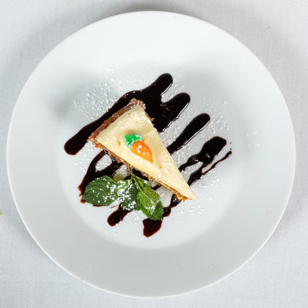 A slice of carrot cake with cream cheese frosting, chocolate drizzle, mint, and powdered sugar.