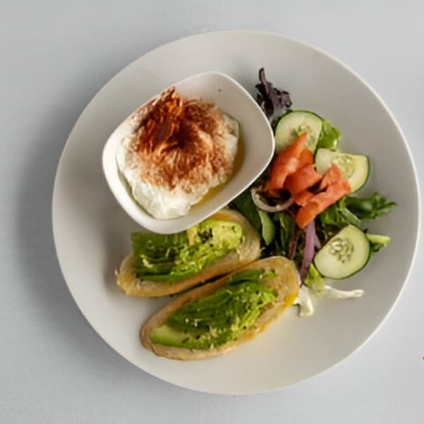 A bistro plate with avocado toast, a side salad, and a bowl of hummus with paprika.