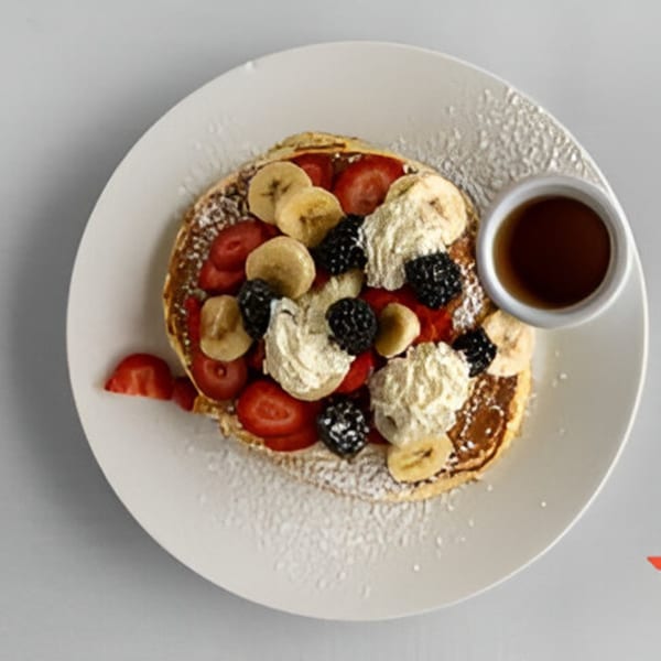 Pancakes topped with strawberries, bananas, blackberries, whipped cream, and powdered sugar, with syrup.