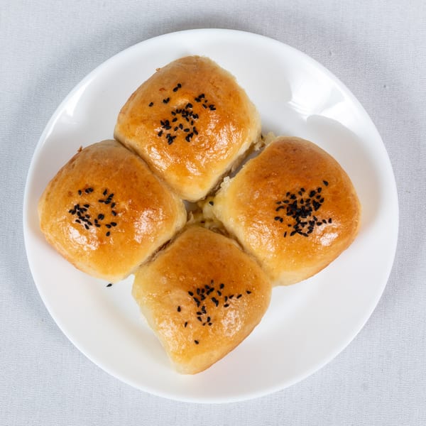 Four golden-brown square pastries, topped with black sesame seeds, arranged on a white plate.