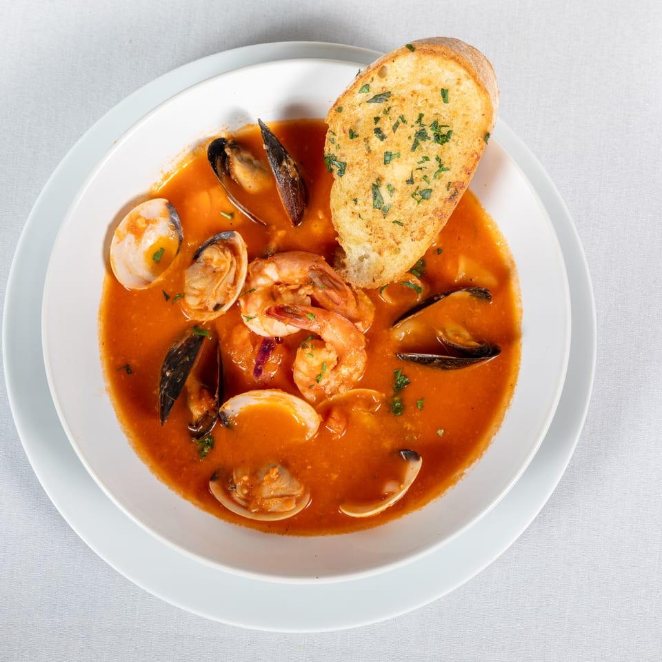 Lighthouse Bistro's seafood cioppino with shrimp, mussels, clams, and garlic bread in a white bowl.