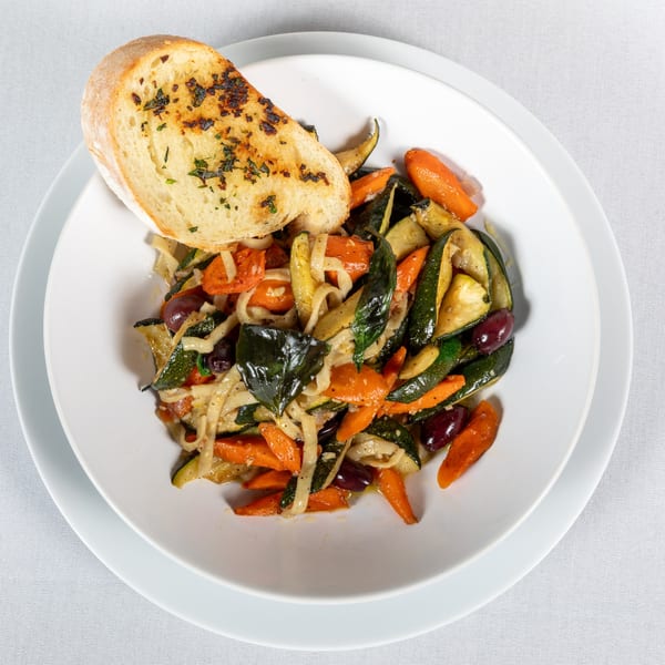 Lighthouse Bistro's vegetable pasta with zucchini, carrots, olives, and garlic bread on a white plate.