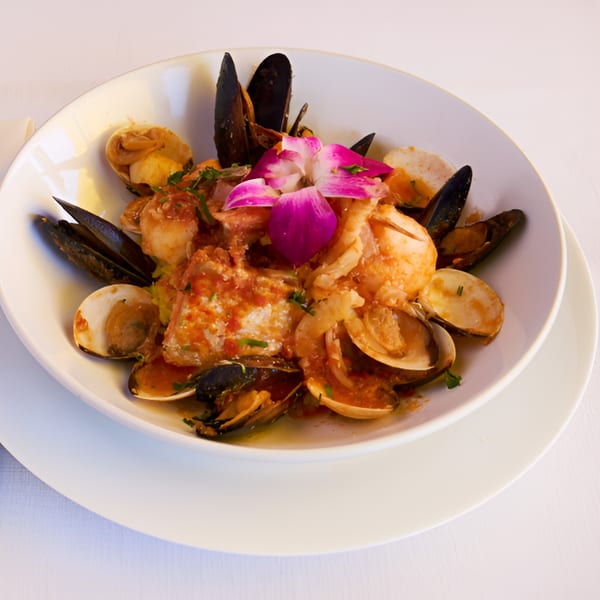 Lighthouse Bistro's seafood dish with mussels, clams, shrimp, and fish in red sauce, garnished with an orchid.
