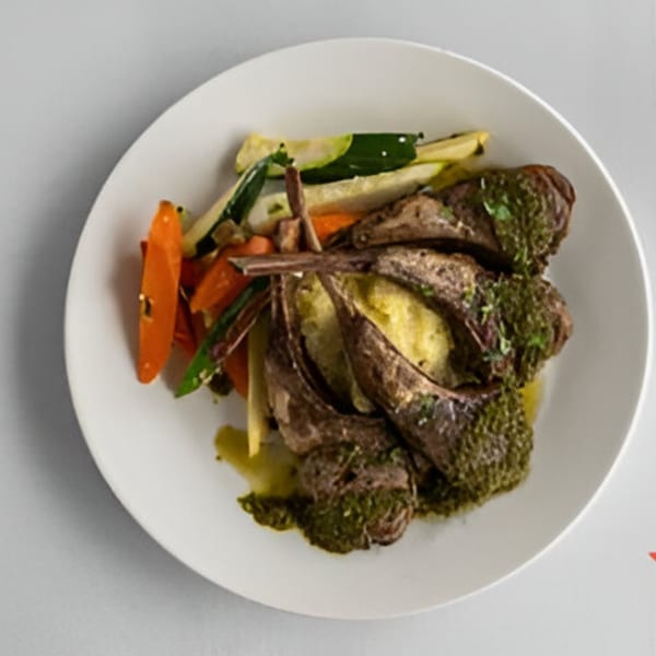 Lighthouse Bistro's lamb chops with mashed potatoes, green sauce, and roasted vegetables on a white plate.