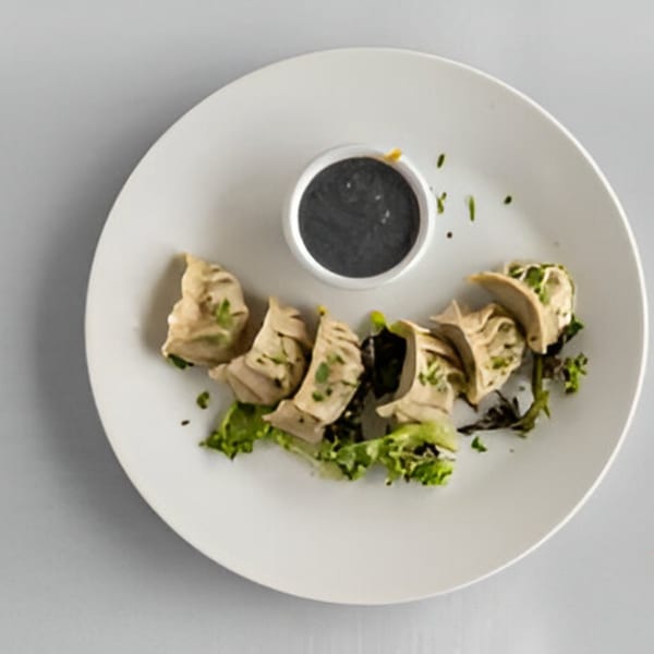 Lighthouse Bistro's dumplings with a dark dipping sauce, garnished with fresh herbs and lettuce.